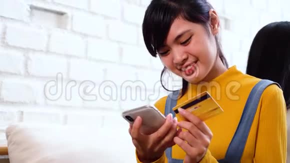 20岁的亚洲少女在舒适的白色房间里拿着信用卡和手机视频的预览图
