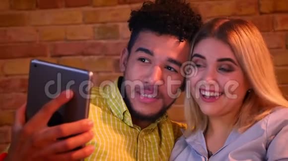 非洲男人和白种人女孩在平板电脑上有一个视频卡在家里快乐地笑着视频的预览图
