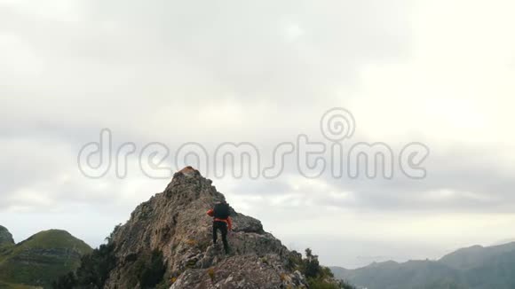 背着背包的年轻女子爬上一座锋利的山脊到达山顶在山顶上的女士视频的预览图