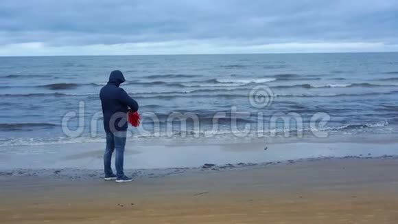 穿着蓝色夹克的人在海滨开着红色的大伞视频的预览图