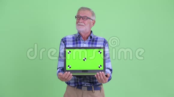 快乐的大胡子时髦男人一边思考一边展示笔记本电脑视频的预览图