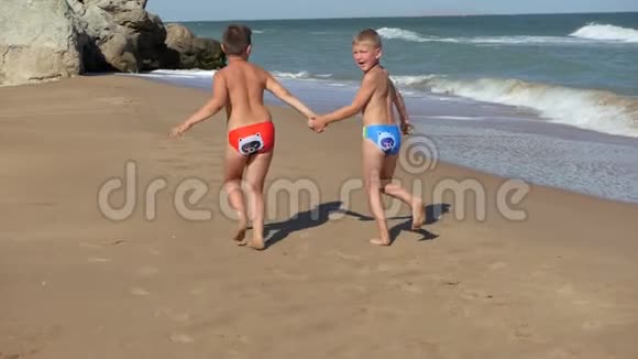 孩子们沿着海岸线奔跑海浪在海滩上冲刷男孩们牵着手沿着海滩奔跑孩子在里面视频的预览图