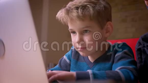 特写镜头拍摄小男孩在笔记本电脑上玩游戏他的母亲坐在附近观察他的活动视频的预览图