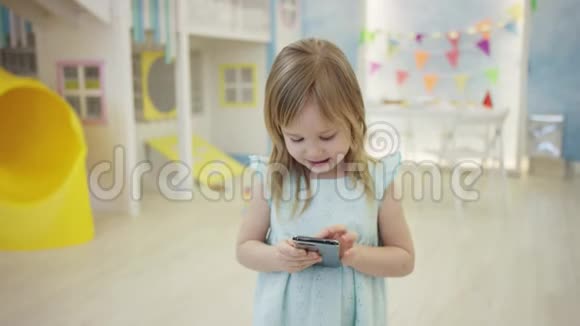 可爱的小女孩正在房间里的摄像机前玩智能手机视频的预览图