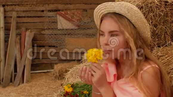年轻迷人的女孩戴着草帽在干草的背景下嗅着一朵黄色的花然后从手掌上吹出花瓣4k4k视频的预览图