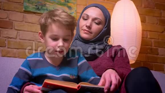 特写镜头集中的小男孩和他的穆斯林母亲在头巾学习如何阅读在家里专心视频的预览图