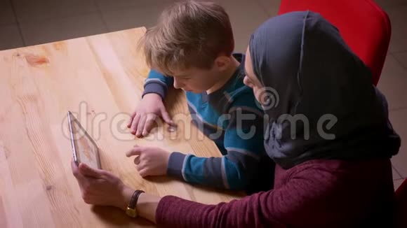小男孩和他的穆斯林母亲戴着头巾在平板电脑上看动画片的照片视频的预览图