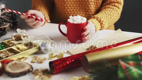 穿着橙色毛衣的女人喝着热巧克力和餐桌上的圣诞礼物视频的预览图