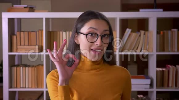时尚的黑发女教师手势的肖像可以在图书馆展示成功视频的预览图