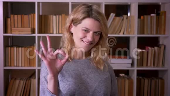 可爱的中年金发老师手势可以标志以显示成功和满意的相机在图书馆视频的预览图