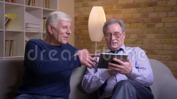资深男性朋友坐在沙发上的画像在平板电脑上滑动照片做出决定视频的预览图