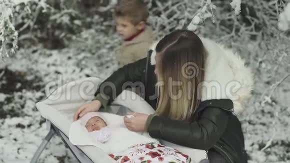 年轻时尚的妈妈和她可爱的女儿和儿子在冬天的雪公园视频的预览图
