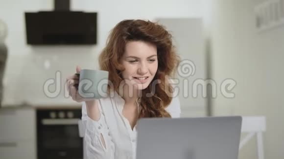 微笑的女人在开放式厨房的电脑上看有趣的新闻视频的预览图