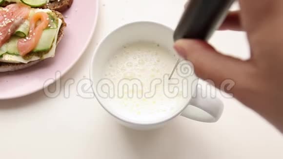 女用手在陶瓷杯中用特殊的搅拌器搅拌卡布奇诺牛奶从上面看视频的预览图