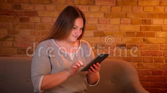 超重长发女性自由职业者在舒适的家庭氛围中愉快地与平板电脑合作的肖像视频的预览图