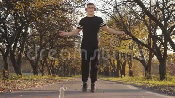 日落时分一位戴着耳机和黑色运动服的高加索青年运动员在秋天公园跳绳的肖像视频的预览图