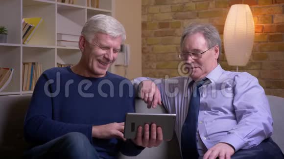 一幅老朋友坐在沙发上在平板电脑上用电玩聊天的特写照片被兴高采烈视频的预览图