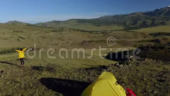 空中特写一个黄色的帐篷矗立在山上夏天女徒步旅行者骄傲地站在山上年轻女子带着视频的预览图