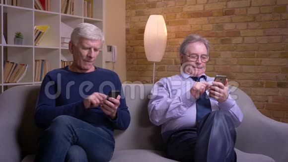 老年男性朋友的肖像互相展示智能手机并愉快地笑视频的预览图