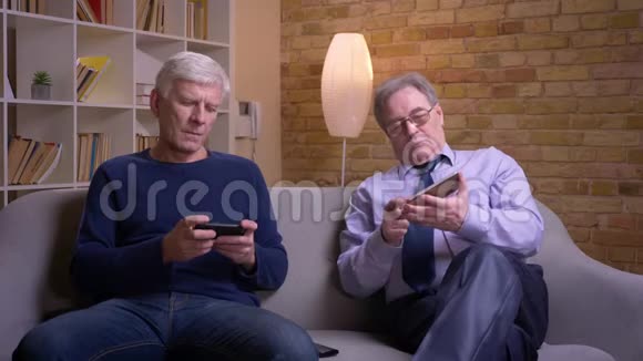 高级男性朋友坐在自己的智能手机里认真而专注地讨论的肖像视频的预览图