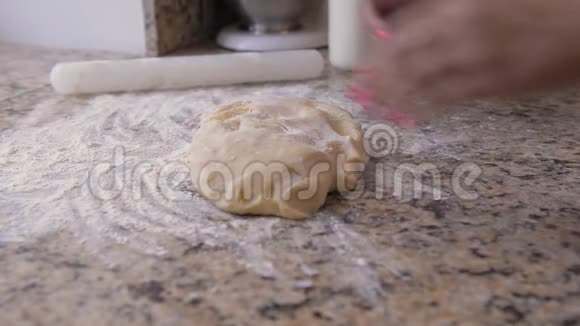 用粉色指甲的女性手用面粉将面团揉在石制台面上视频的预览图