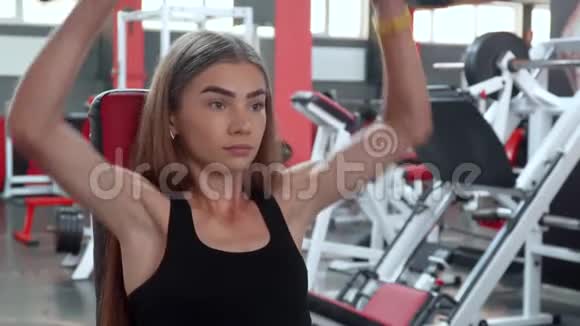 年轻的健身妇女在健身房锻炼哑铃坐在长凳上视频的预览图