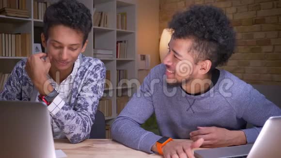 印度和非裔美国男学生使用笔记本电脑和讨论学校工作坐着的特写镜头视频的预览图