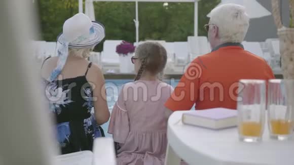 祖母祖父和孙子坐在豪华游泳池的边缘友好的家庭休息视频的预览图