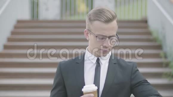 一幅年轻英俊衣着考究戴着眼镜端着咖啡站在楼梯前的商人画像这就是视频的预览图