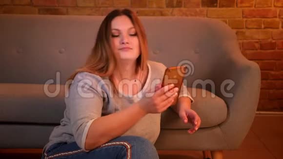 超重的长发女性自由职业者坐在地板上与智能手机在舒适的家庭氛围视频的预览图