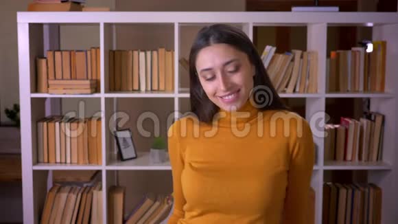 时尚的黑发女教师的肖像在镜头中快乐地微笑着在图书馆里调情视频的预览图