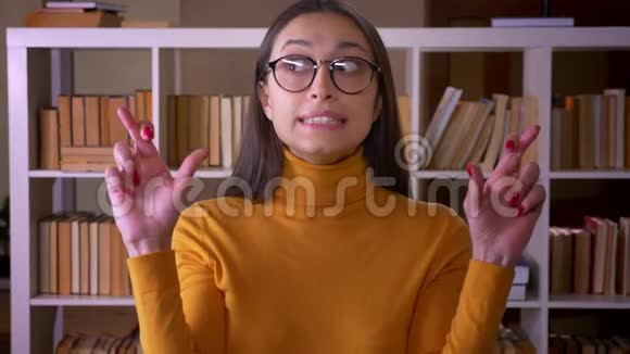 一幅时尚的黑发女教师与交叉手指祈祷的肖像希望在图书馆好运视频的预览图