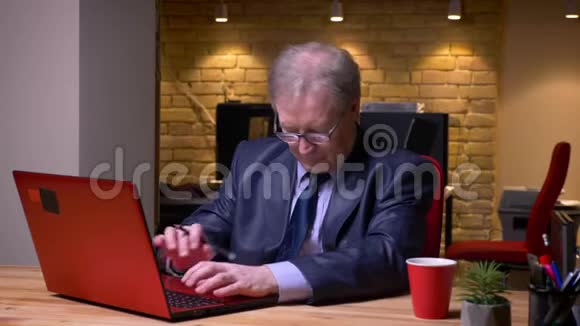 穿着正式服装的老人在笔记本电脑上打字和在笔记本上写笔记的肖像集中在办公室视频的预览图