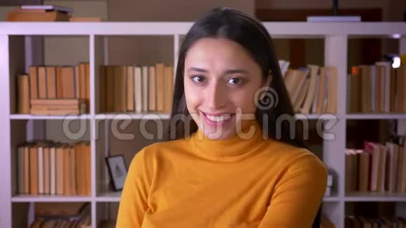 一幅美丽的黑发女教师的肖像在镜头中欢快地微笑着在图书馆里调情视频的预览图