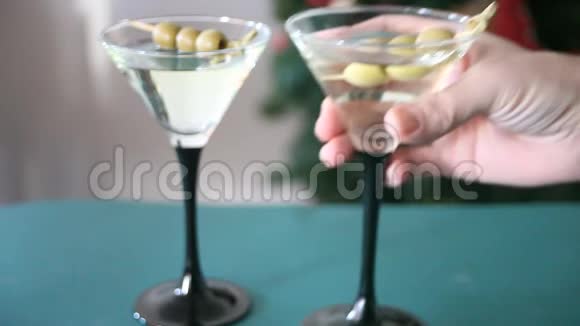 女人的手放在蓝色的桌子上一杯带橄榄的马提尼视频的预览图