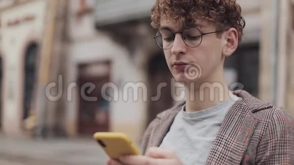 用他的现代智能手机设备特写眼镜中的年轻学生的肖像在屏幕上滚动视频的预览图
