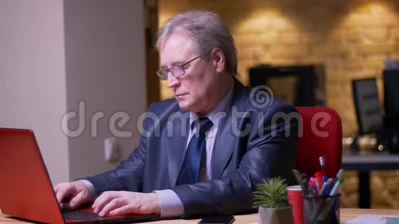 高级商人的肖像穿着正式服装在办公室同时使用笔记本电脑和智能手机视频的预览图