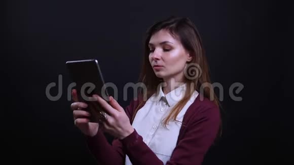 年轻的黑发女商人在黑色背景下愉快地在平板电脑上制作漂亮的自拍照片的肖像视频的预览图