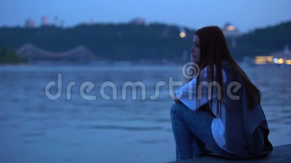 坐在河堤上享受平静的水和清新的傍晚空气的愤怒女孩视频的预览图
