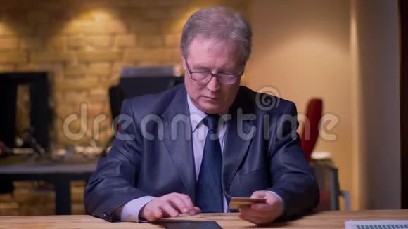 高级商人在正式服装制作交易与信用卡和平板电脑在办公室的肖像视频的预览图