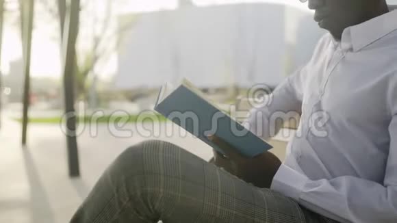 戴眼镜的年轻非洲学生坐在公园里看书视频的预览图