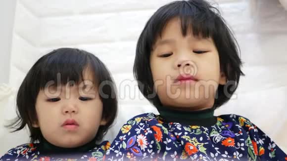 两个亚洲小女孩姐妹全都在家看智能手机视频的预览图