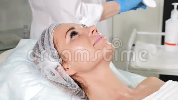 美容院女性美容师在面部护理前用湿棉布垫清洁女性皮肤的特写镜头视频的预览图