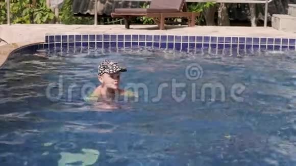 穿着袖子和帽子的小男孩正在度假时在游泳池里游泳男孩在热带的游泳池里游泳视频的预览图