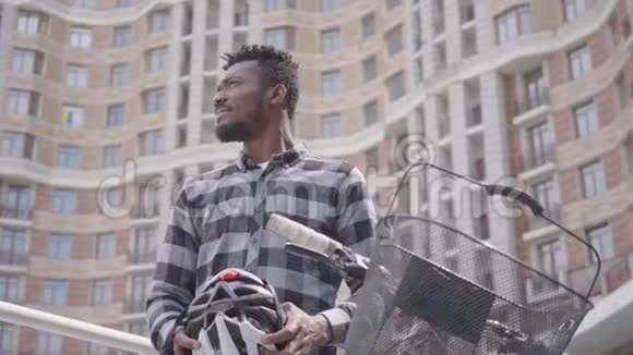 英俊的非裔美国人手里拿着自行车站在高楼大厦前手里拿着自行车头盔视频的预览图