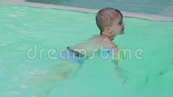 穿着袖子和帽子的小男孩正在度假时在游泳池里游泳男孩在热带的游泳池里游泳视频的预览图