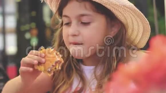 可爱的饥饿的小女孩带着草帽微笑着吃她的奶酪汉堡视频的预览图