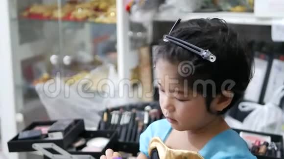 可爱的亚洲小女孩一边玩化妆海绵一边接受专业化妆视频的预览图