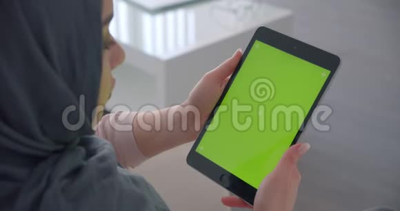 穆斯林女商人戴着头巾看着平板电脑绿色的彩色屏幕沉浸在扶手椅上工作视频的预览图