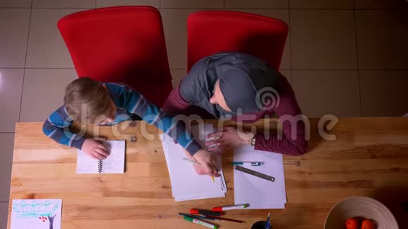 头号镜头的穆斯林母亲戴着头巾和她的小儿子在家里的桌子上做作业视频的预览图